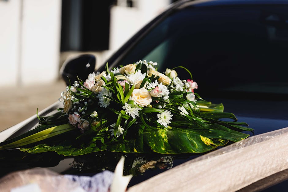 A fresh floral arrangement featuring a bouquet of predominantly white and soft pink roses, white daisies, and small white filler flowers, all arranged with lush green foliage and long leafy stems. The
