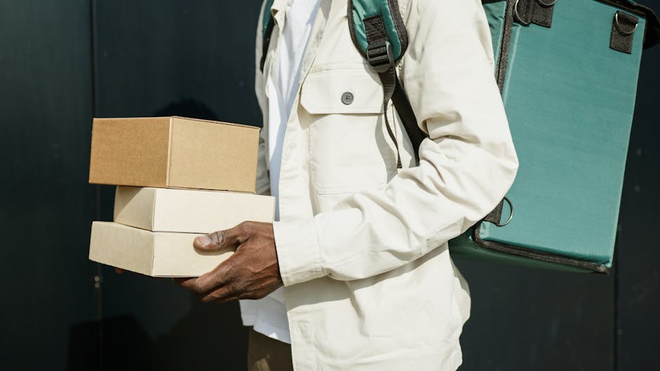 A person holding three rectangular boxes of varying sizes, stacked one on top of the other, with the top box being brown and the lower two boxes in white. The individual is dressed in a light-colored 